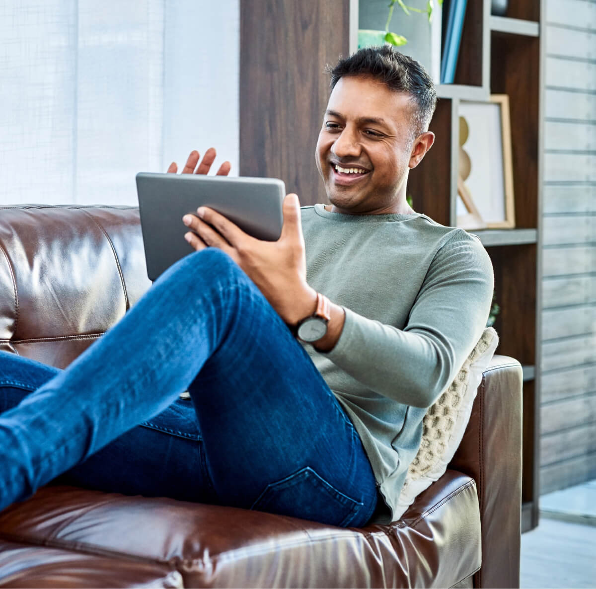 Man lounging on a couch while scrolling on tablet