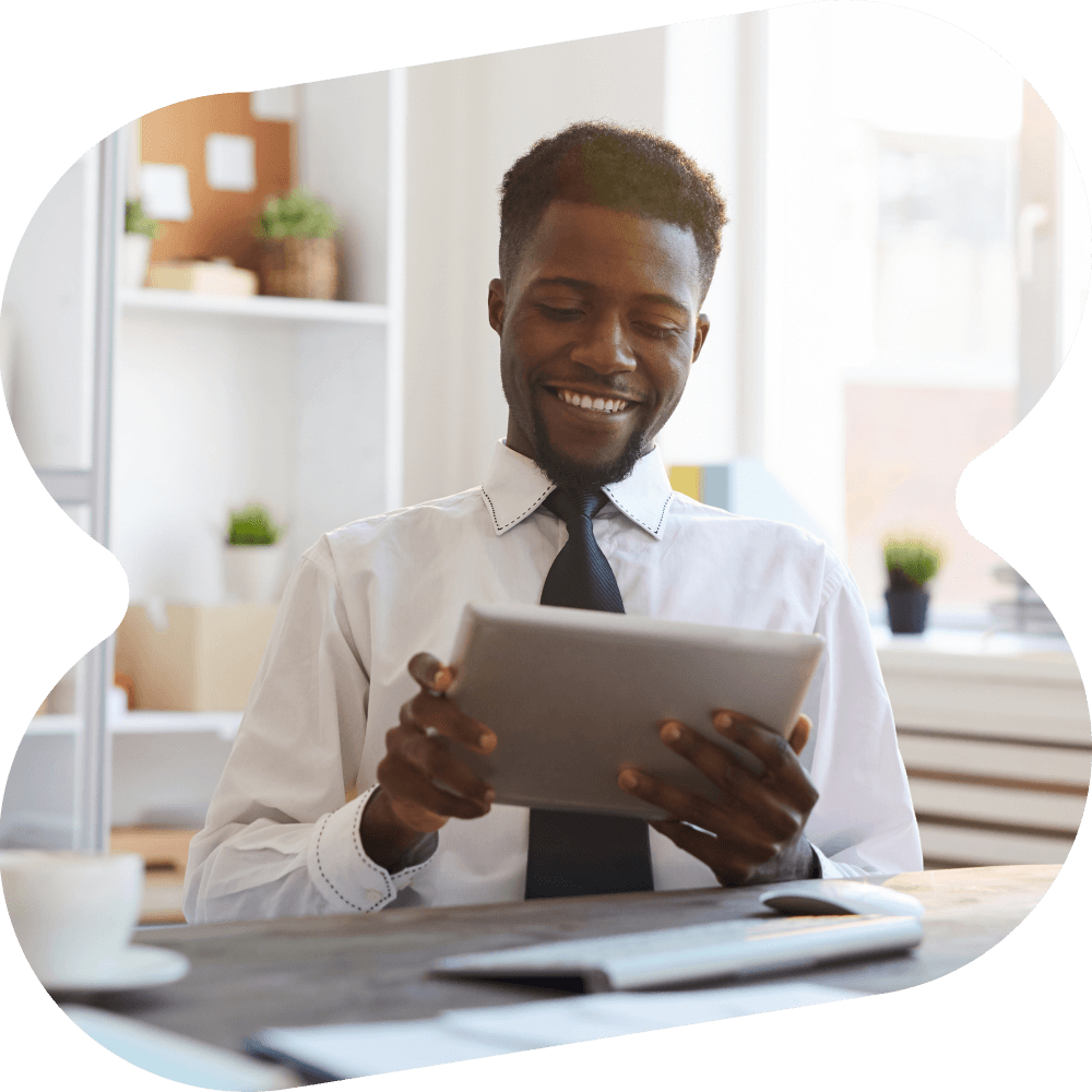 Man sitting at a desk, reading a tablet and smiling