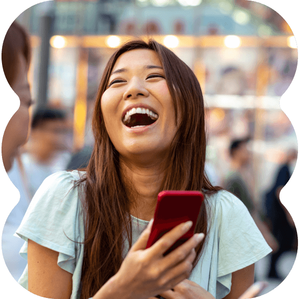 Two girls laughing together while outside, holding cell phones