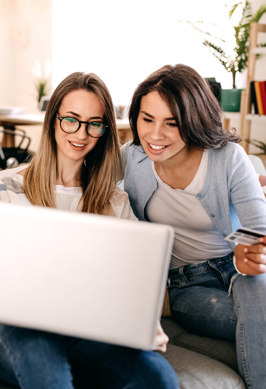 Two women on couch holding a credit card and laptop