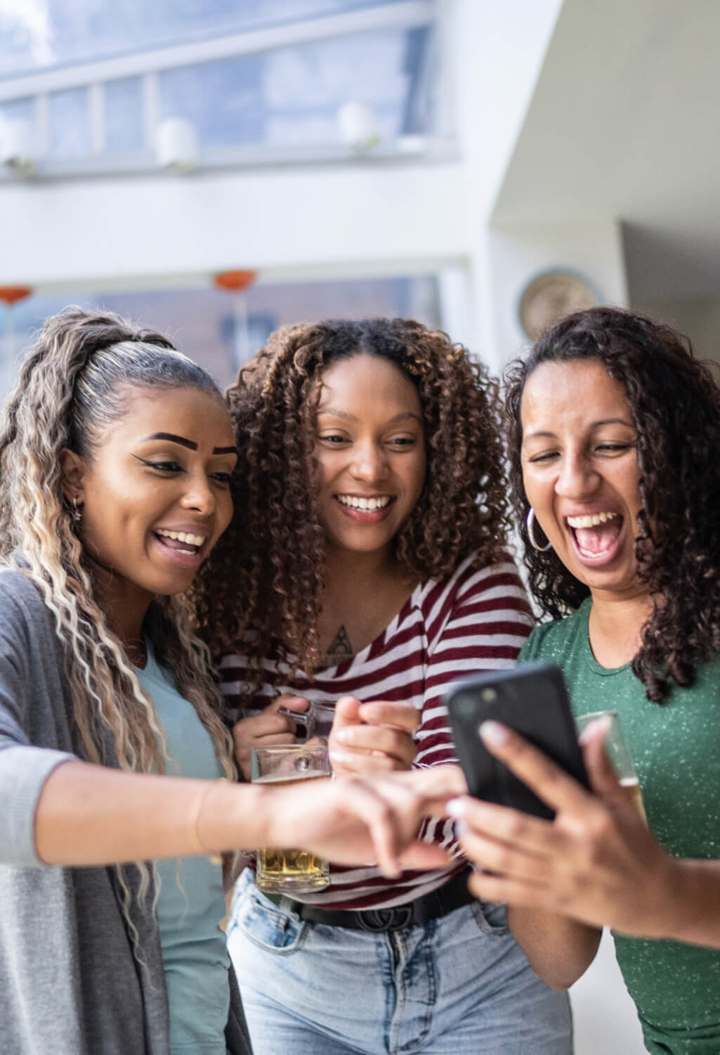 Three friends holding drinks, laughing at phone