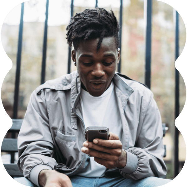 Young man looking down on his phone while sitting outside on a city bench.